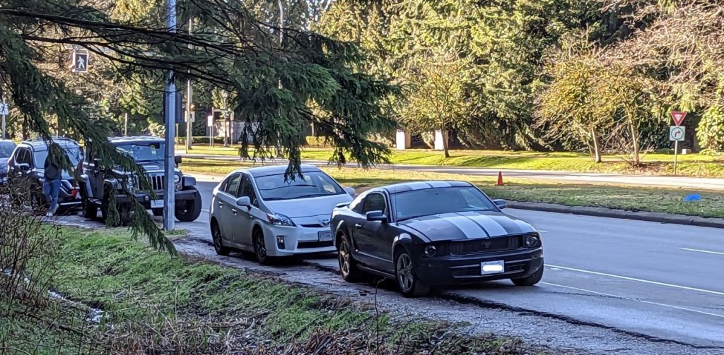 Auf einer Strasse in Vancouver parken an der Seite Autos. Im Vordergrund ist ein schwarzer Ford Mustang mit zwei weissen Streifen in der Mitte zu sehen.