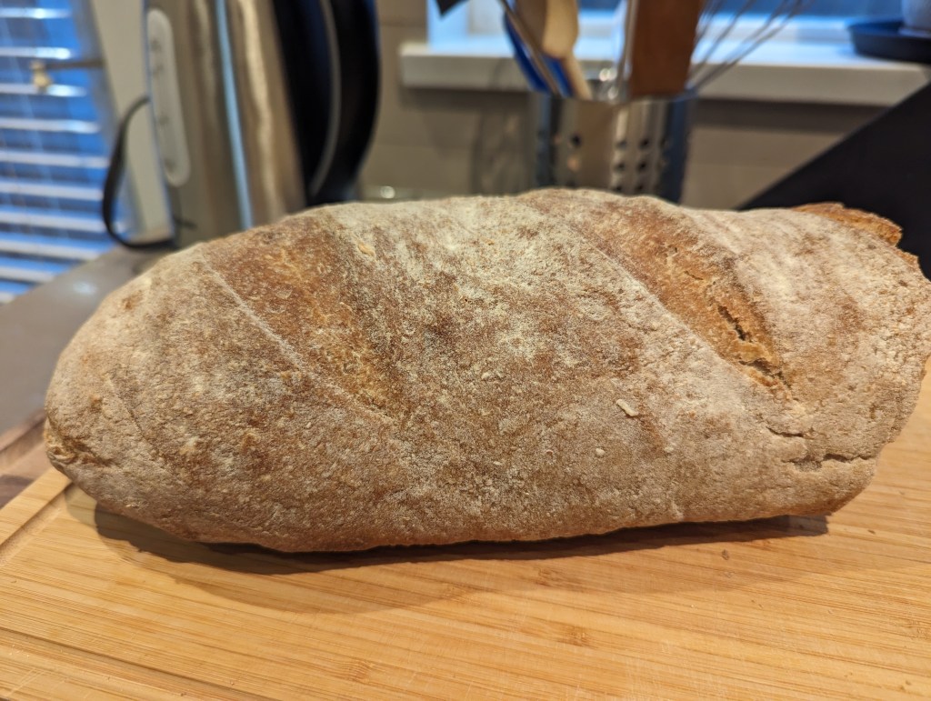 Ein bereits angeschnittenes Roggenbrot deutscher Art liegt auf einem Holzbrett.