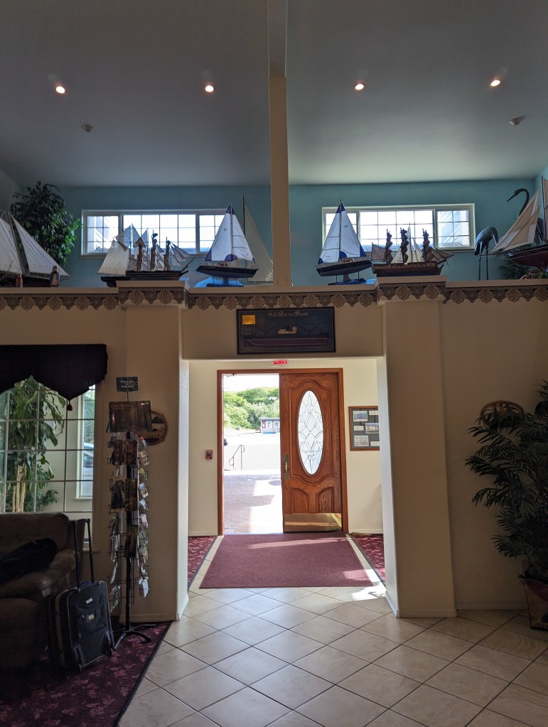 Das Innere eines Hotels in Crescent City. Man sieht die Eingangstür von innen, über der Tür des Empfangsraums gibt es eine Ballustrade, auf der kleine Modellboote stehen.