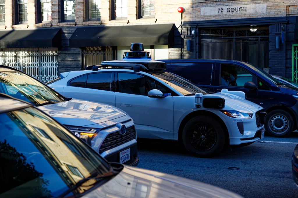Man sieht ein weißes selbstfahrendes Auto auf einer Straße, von der Seite fotografiert.