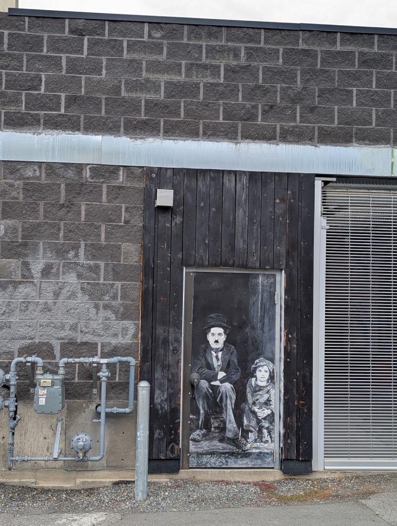 Ein Mural an einer Hauswand.  Zu sehen ist ein sitzender Charlie Chaplin, neben ihm sitzt ein Mädchen.