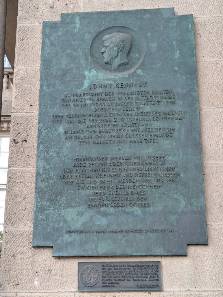 John F. Kennedy
35. Präsident der Vereinigten Staaten von Amerika sprach in der Mittagsstunde des 26. Juni 1963 an dieser Stätte zu den Bürgern Berlins
Hier versammelten sich in der Nacht des 22. November 1963 die Berliner zur Totenklage für den ermordeten Staatsmann
In Dank und Ehrfurcht enthüllten sie am 26. Juni 1964 ihrem großen Freunde zum Gedächntis diese Tafel
~
Miteinander werden wir unsere Erde retten oder miteinander in den Flammen ihres Brandes umkommen
Aber retten können und retten müssen wir sie und damit werden wir uns den ewigen Dank der Menschheit verdienen und als Friedensstifter den ewigen Segen Gottes
(John F. Kennedy in seinem Appell an die Völker, 25. September 1961)