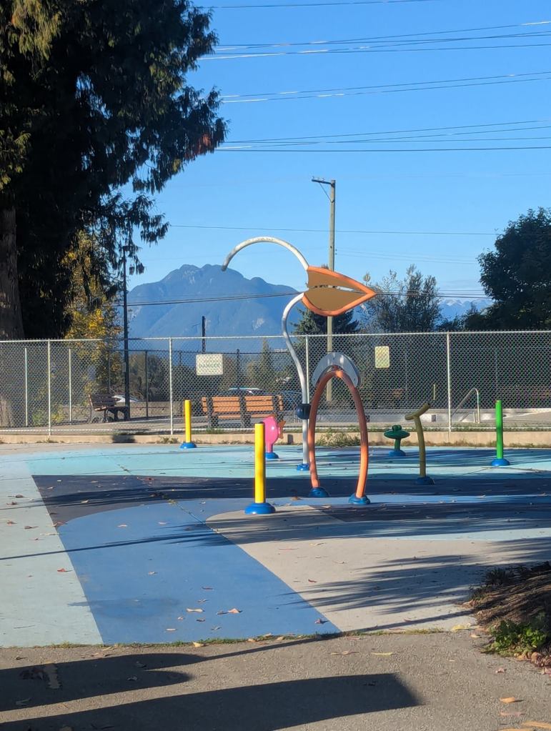 Ein moderner Spielplatz mit verschiedenen bunten Geräten. Im Hintergrund sieht man Berge.