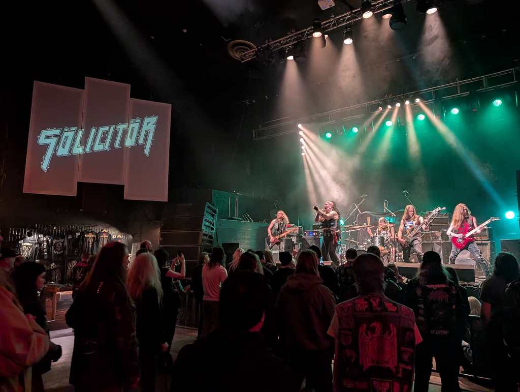 Die Band Sölicitör steht auf der Bühe und performt. Davor stehen einige Zuschauerinnen und Zuschauer.