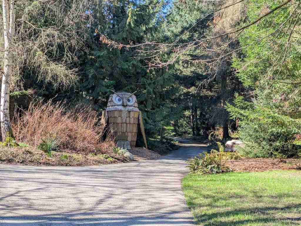 Eine große, hölzerne Eule steht am Wegesrand.