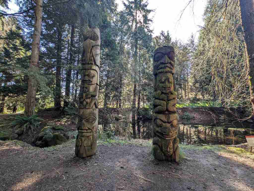 Totem-Pfähle stehen an einem Flussufer.