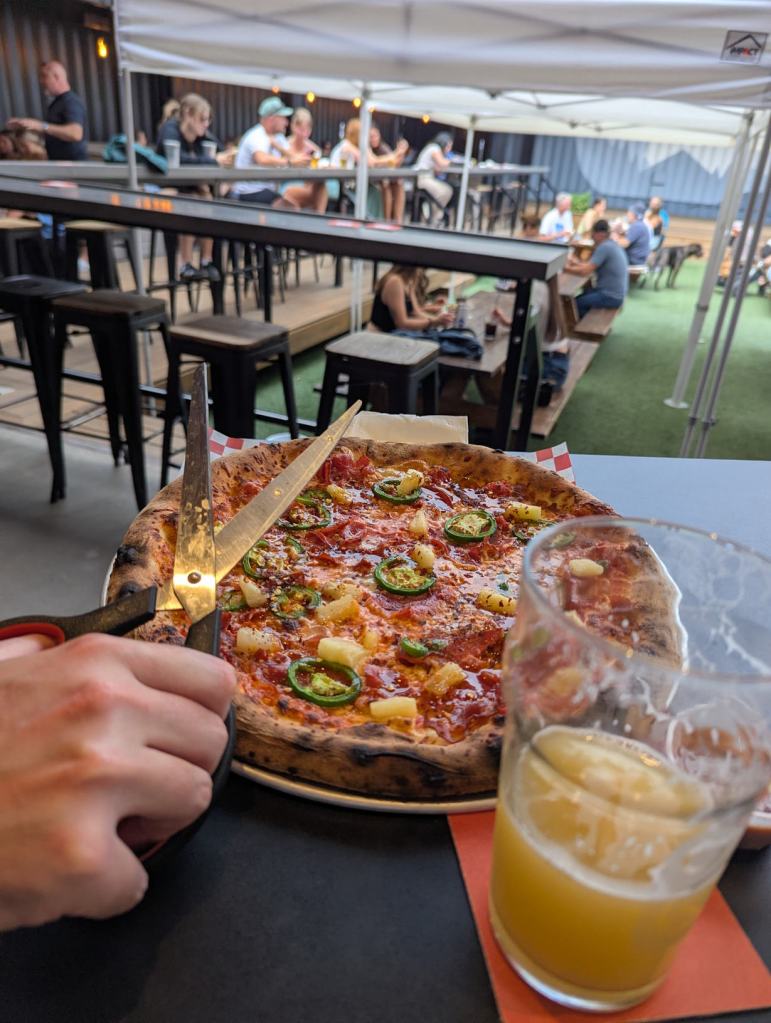 Eine Pizza wird mithilfe einer Schere in Stücke geschnitten. Eine Pizza wird mithilfe einer Schere in Stücke geschnitten.