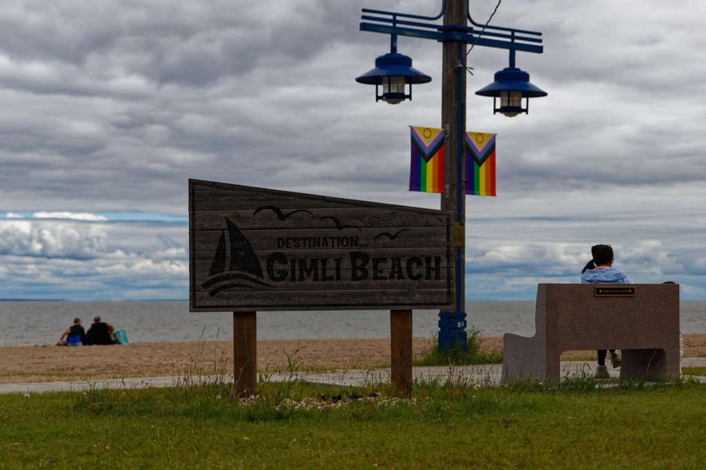 Ein Strand mit Schild "Gimli Beach" sowie einer Pride-Flagge an einer Lampe