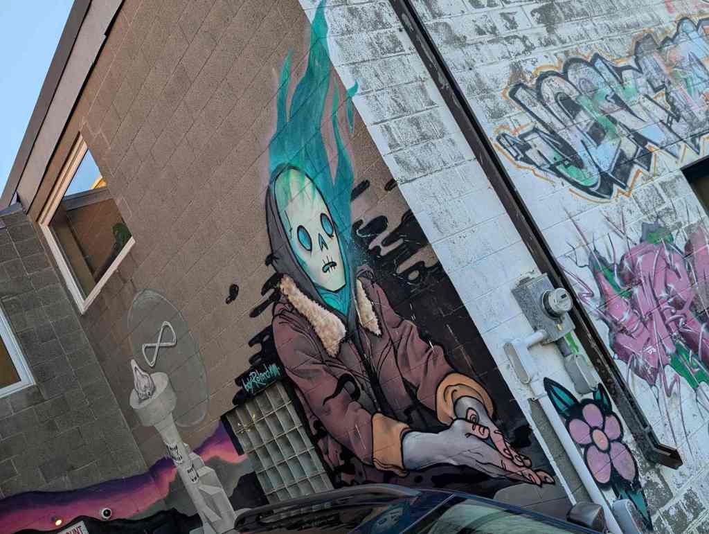 Ein buntes Mural mit einer Person, die ein geistartiges Gesicht hat, aus dem blaue Flammen kommen. Es sieht horrormäßig aus.