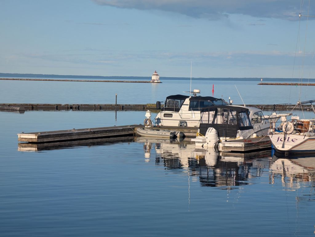 Boote sind an Stegen festgetaut. In der Ferne sieht man einen kleinen Leuchtturm.