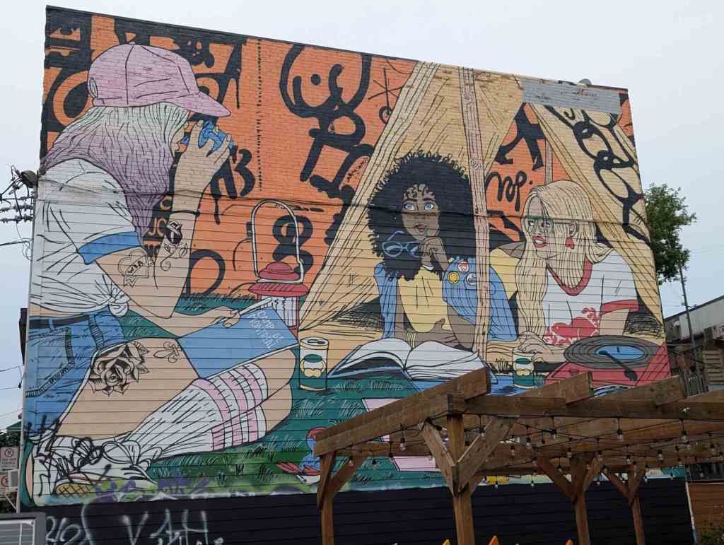 Mural von drei verschiedenen lesenden Frauen, die einander zugewandt sind..