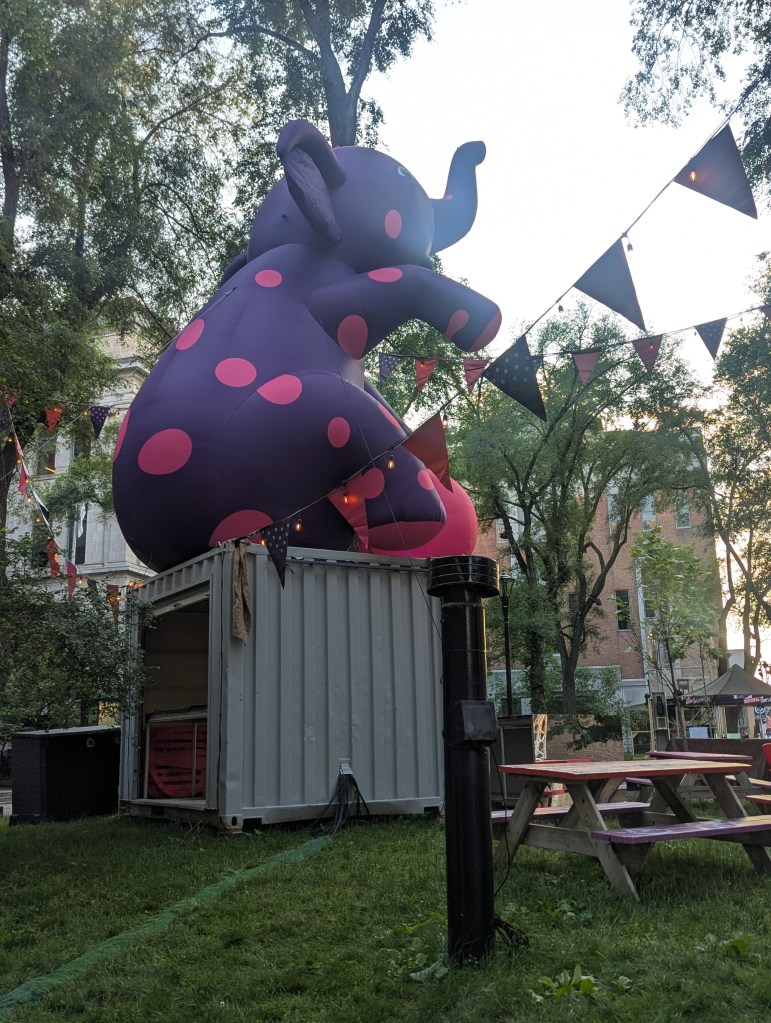 Die aufblasbare Skulptur eines lilafarbenen Elefanten mit pinken Punkten sitzt auf einem grauen Container.