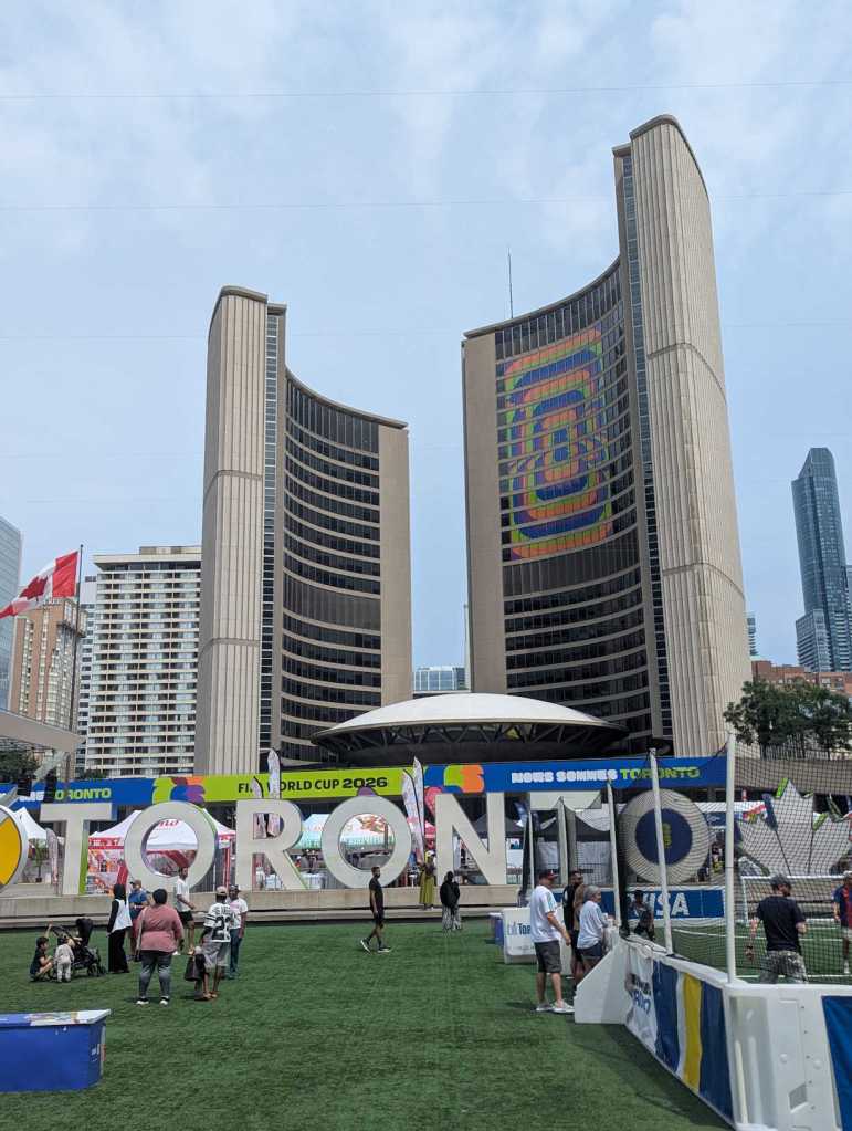 Zwei hohe halbförmige, aus Beton bestehende, Gebäudeteile, in denen Büros untergebracht sind. Sie rahmen ein, wie eine Untertasse aussehendes Gebäude, ein. Davor steht der Toronto-Schriftzug auf Kunstrasen.