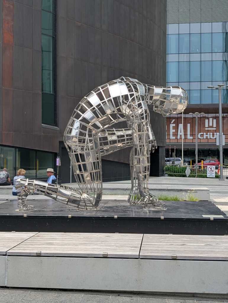 Skulptur einer silbernen knieenden Figur.