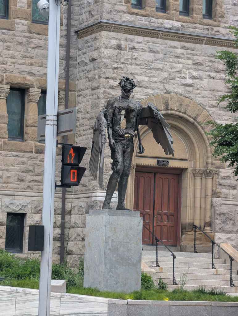 Die Skulptur einer zunächst menschlich anmutenden Figur mit Flügeln, in dessen Mittelbereich - was bei einem Menschen der Bauch und Teile der Brust wären - ein großes Stück fehlt und man hindurch gucken kann.
